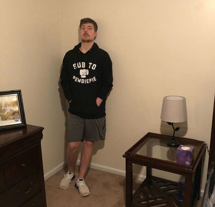 a man is standing in the corner of his room next to a dresser and lamp