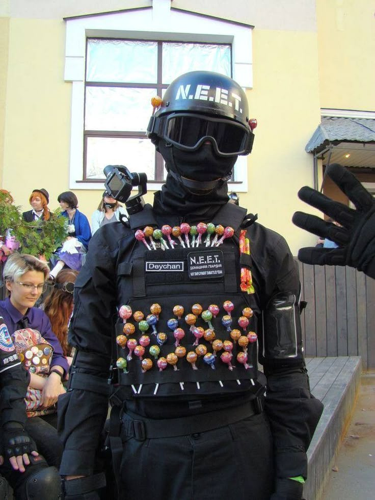 a man in a black suit and helmet with beads on his chest standing next to a group of people