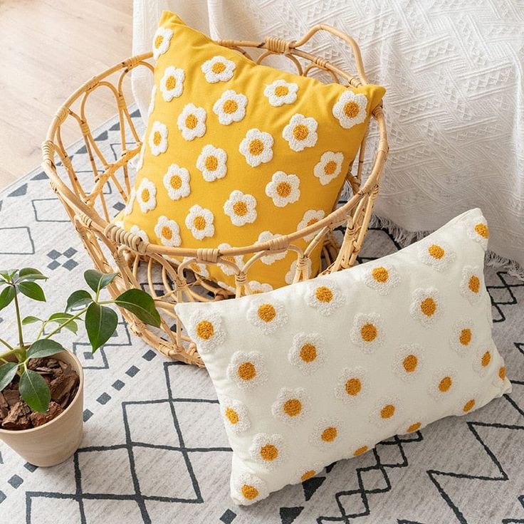 two yellow and white pillows sitting on top of a rug next to a potted plant