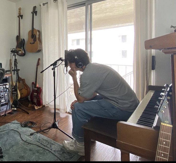 a man sitting in front of a piano with headphones on and an instrument next to him