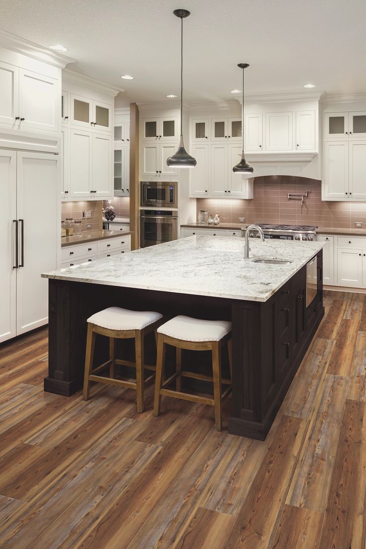 a large kitchen with white cabinets and wood flooring, two stools on the island