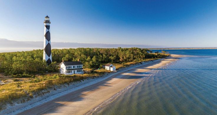 an aerial view of a lighthouse on the beach with trees and water in the background