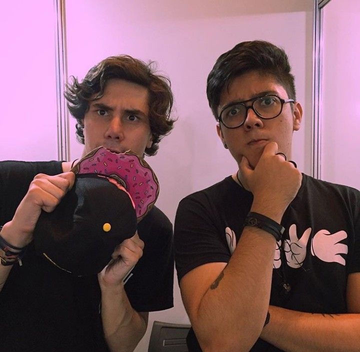 two young men are brushing their teeth in front of a mirror, one is holding a doughnut