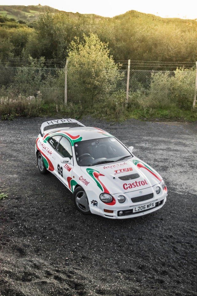 a white car with red and green stripes parked in a gravel lot next to trees