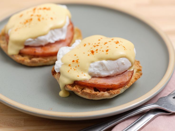 two english muffins on a plate with cream sauce and bacon, next to a fork