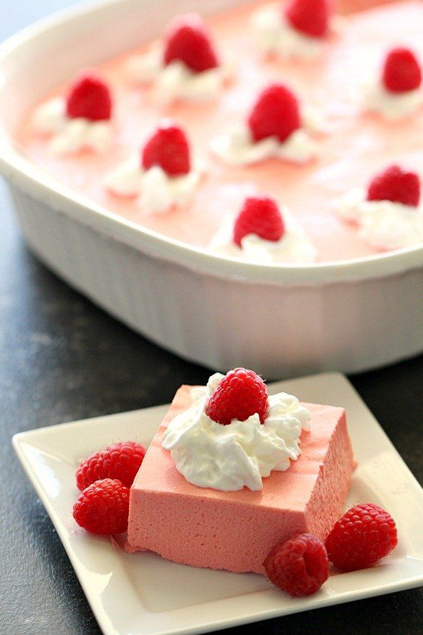 a piece of cake with raspberries and whipped cream on top sitting on a plate