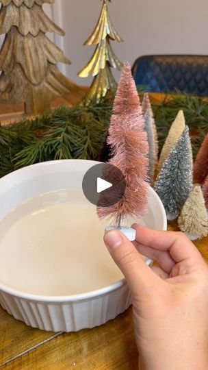 someone is decorating small christmas trees in a bowl on a table with other ornaments