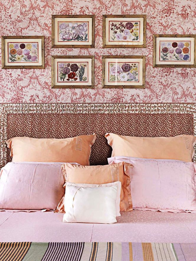 a bed with pillows and pictures on the wall above it in a room that has pink walls