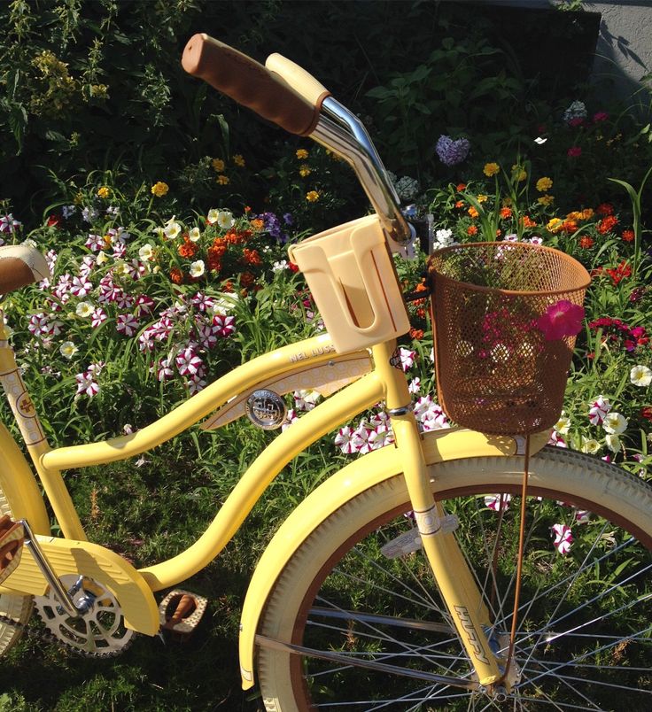 a yellow bicycle is parked in the grass near some flowers and other colorful flowers, with a basket on the front