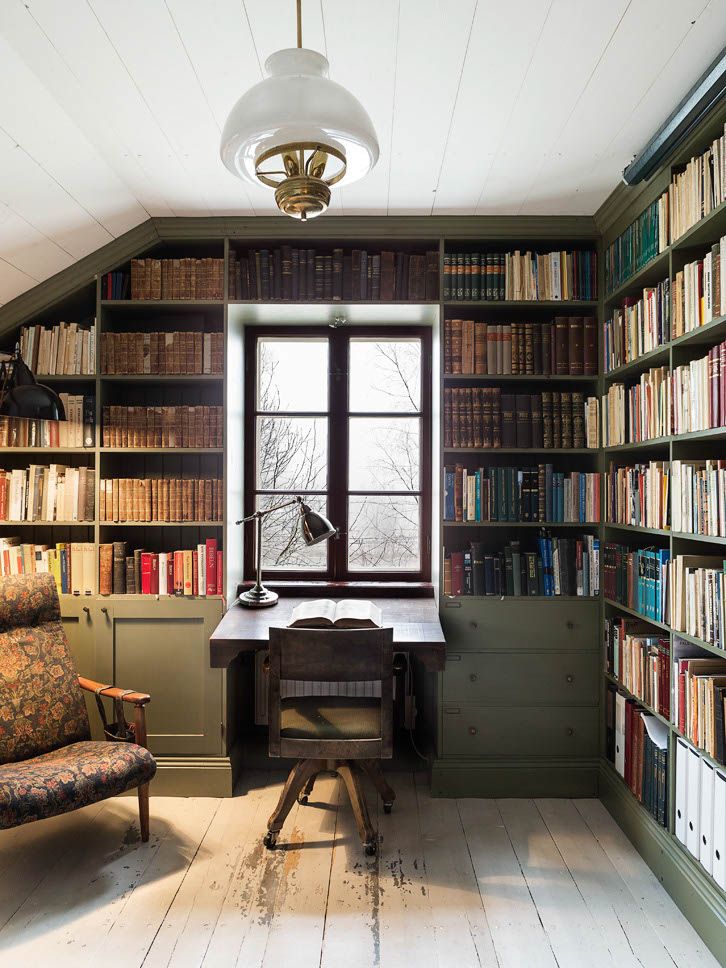 a room with bookshelves and a desk in the corner, next to a window