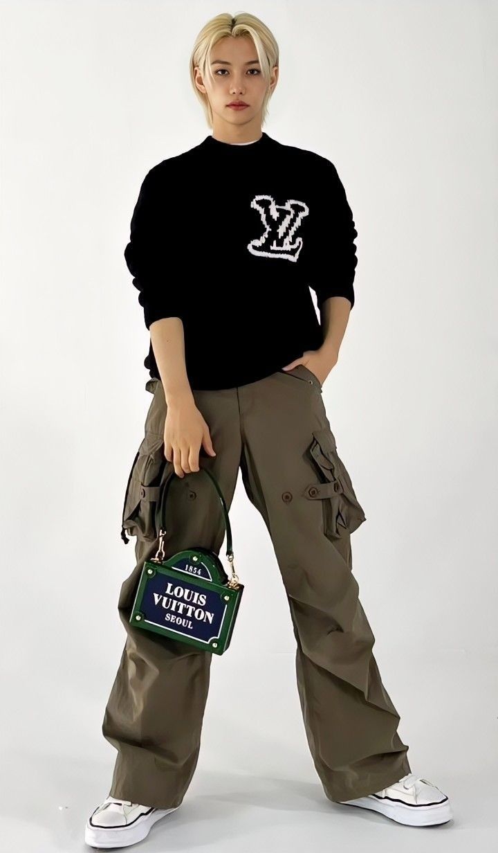 a woman with blonde hair wearing cargo pants and a black sweatshirt holding a green bag