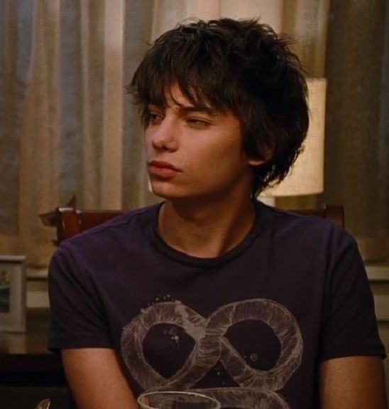 a young man sitting at a table with a glass in front of him and looking off to the side