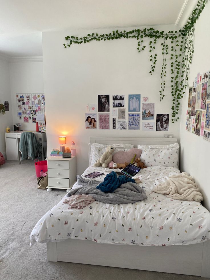 an unmade bed in a white bedroom with lots of pictures on the wall above it