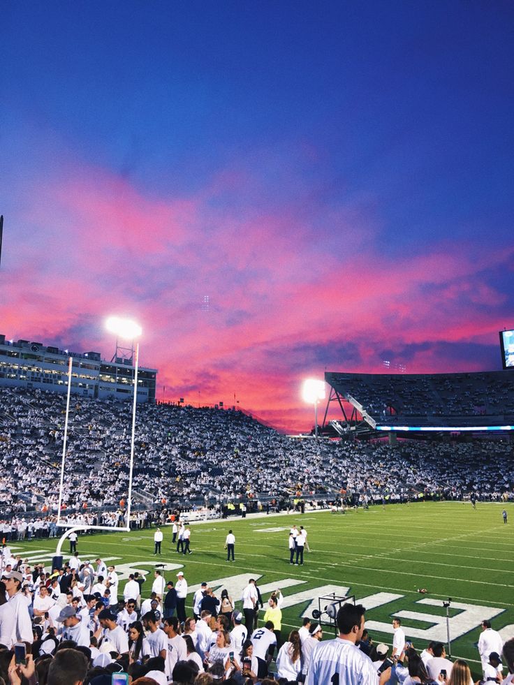 a stadium filled with lots of people watching a football game at sunset or sunrise time