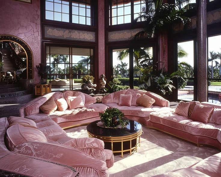 a living room filled with lots of pink couches and furniture in front of large windows