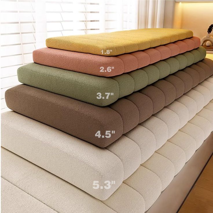 four different colors of pillows stacked on top of each other in front of a window