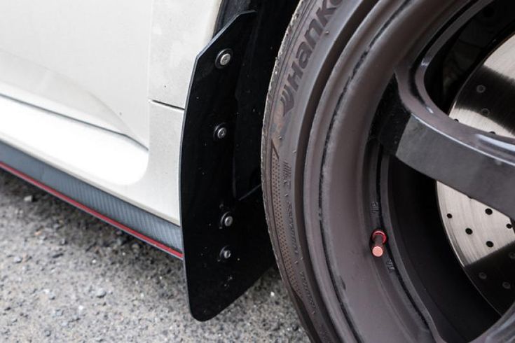 the front wheel of a white car with black rims and red brake pads on it