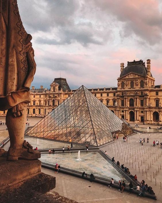 people are standing around in front of a large building with a pyramid on it's side