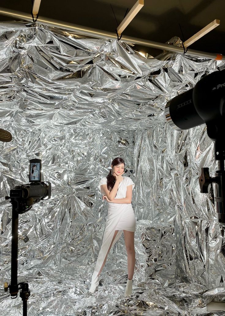 a woman standing in front of a silver foil backdrop with a camera and tripod