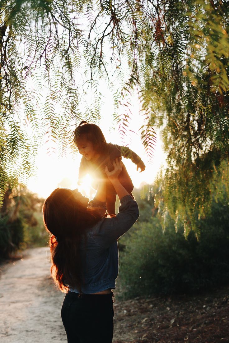 a woman holding a baby up to her face while walking down a path in the woods