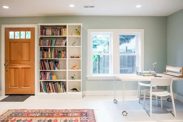 a living room filled with furniture and a book shelf next to a window on top of a rug