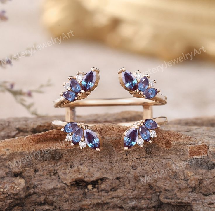 two gold rings with blue and white stones on them sitting on a piece of wood