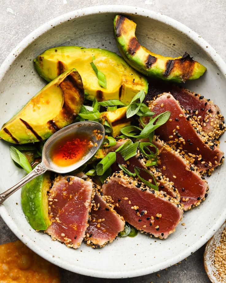 a white plate topped with meat and veggies next to sliced avocado