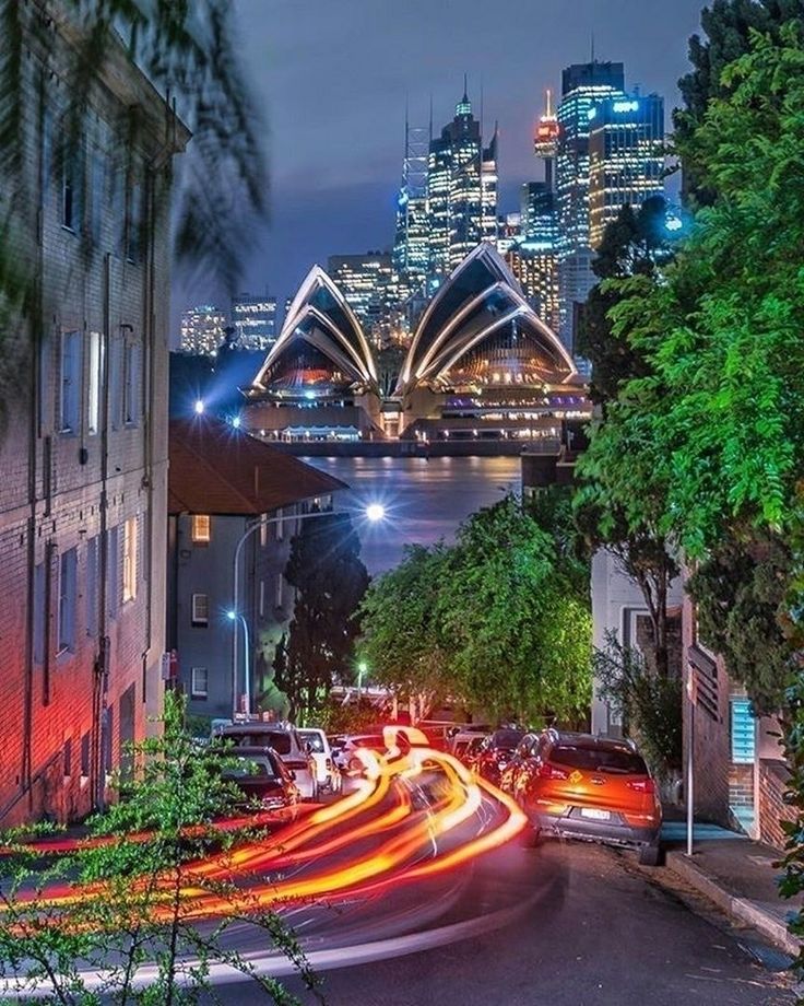 the city skyline is lit up at night with light streaks on the street and cars driving down the road