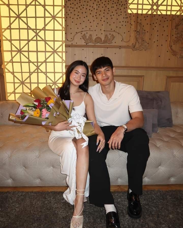 a man and woman sitting on a couch holding flowers