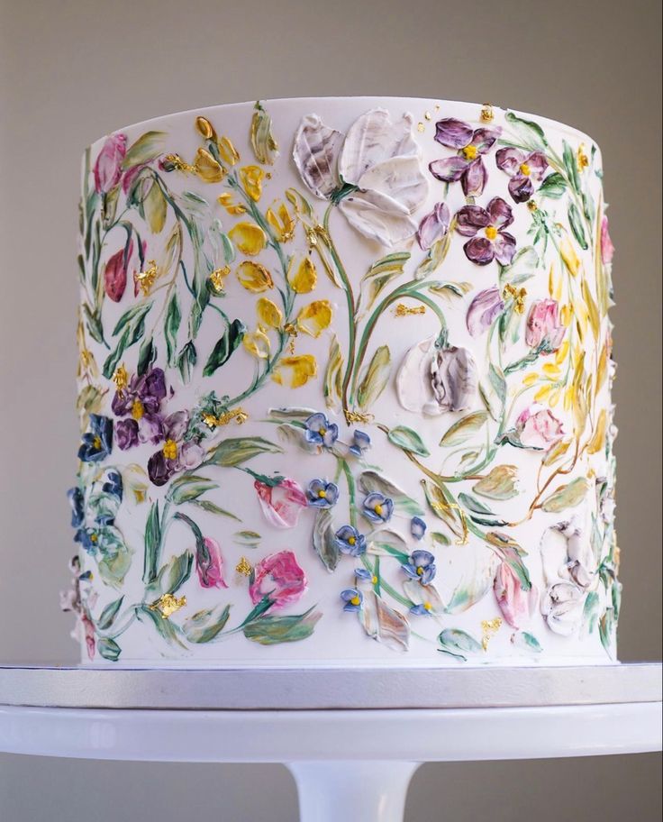 a white cake decorated with flowers and leaves on top of a stand in front of a wall