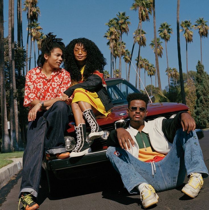 two women and a man sitting on the back of a car in front of palm trees