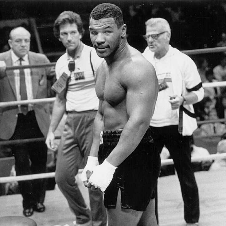 a black and white photo of a man with boxing gloves standing in front of two men