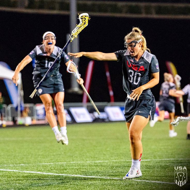 two women playing lacrosse on a field at night