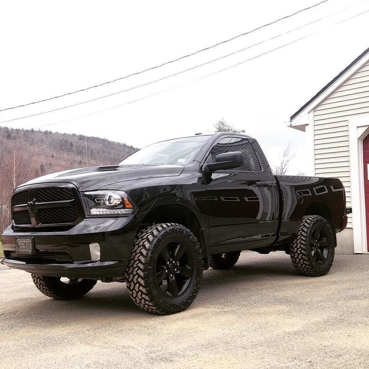 a black ram truck parked in front of a garage with a red door behind it