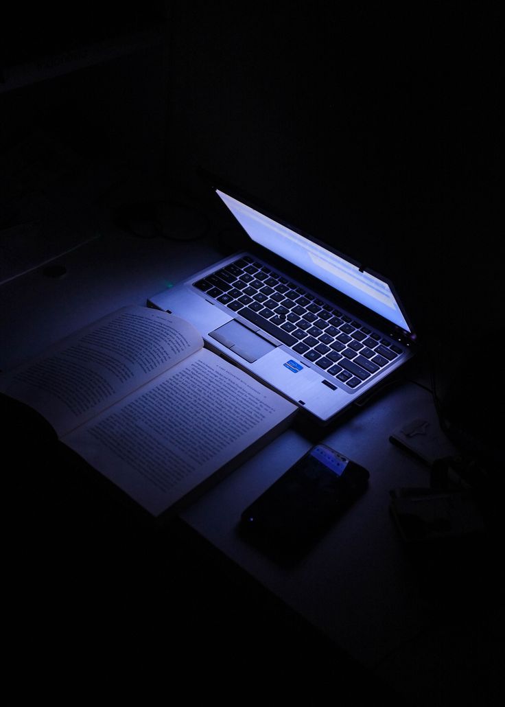 an open laptop computer sitting on top of a desk next to a book and cell phone