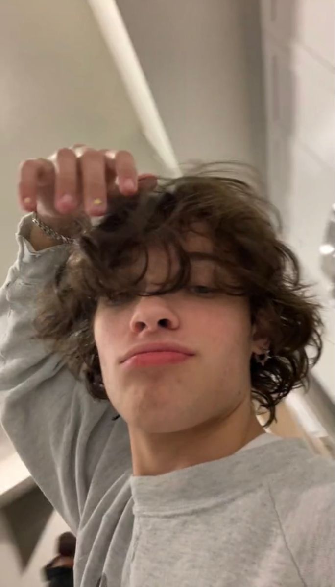 a young man with curly hair holding his hands up to his head