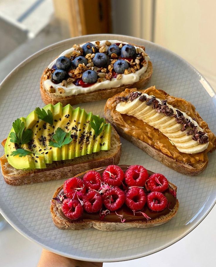 four slices of bread with fruit and nuts on them are displayed on a white plate