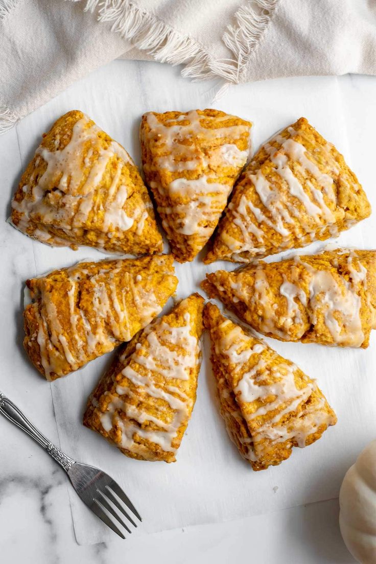 pumpkin scones with icing on a white plate next to a knife and fork