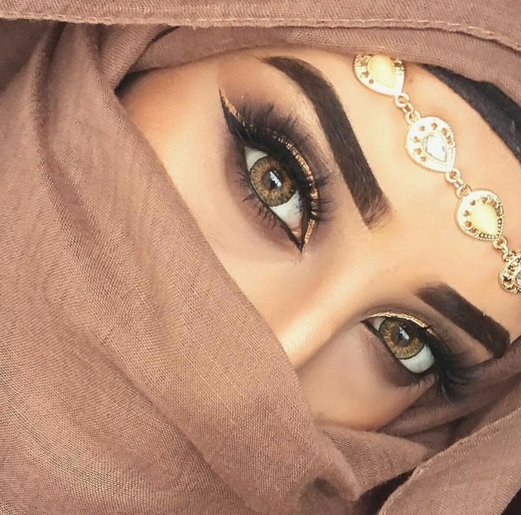 a close up of a woman with brown eyes and gold jewelry on her head, wearing a hijab