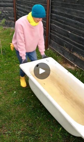 a person in a pink sweater and yellow rubber boots cleaning a white bathtub outside