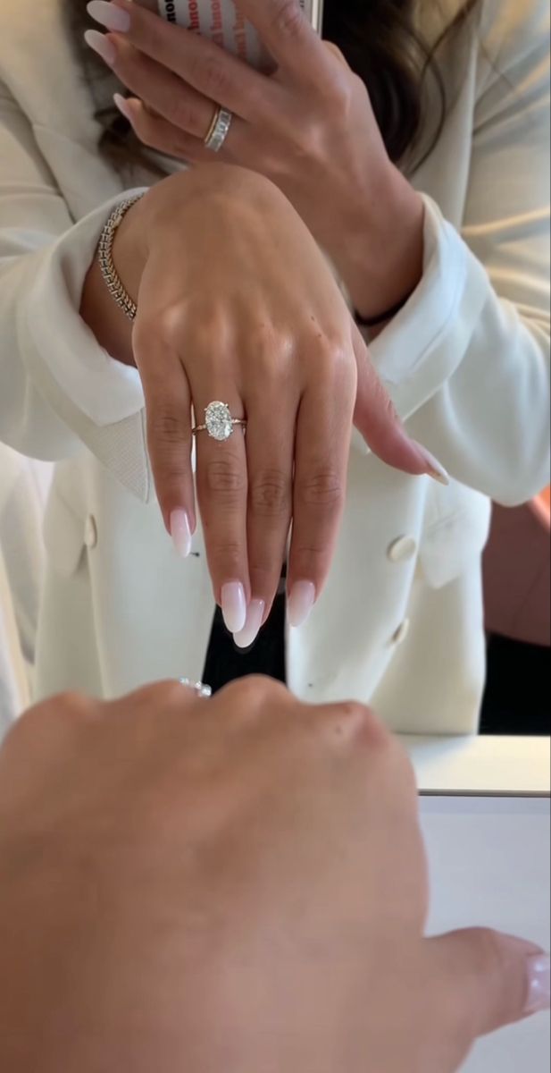 the woman is looking at her cell phone while wearing a white suit and diamond ring