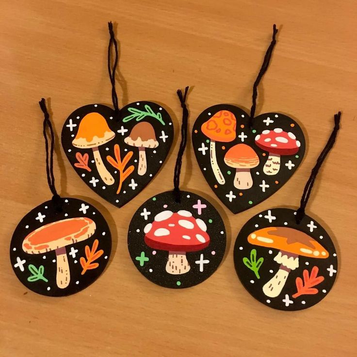 four heart shaped ornaments with mushrooms and stars painted on them, sitting on a wooden surface