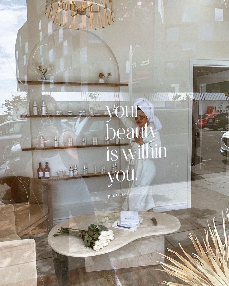 there is a display in the window of a beauty shop that has flowers and bottles on it