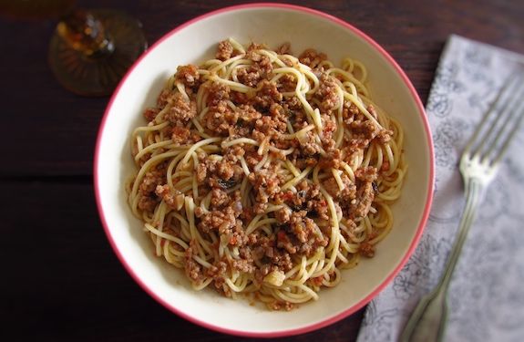 a bowl filled with spaghetti and meat on top of a table next to a fork