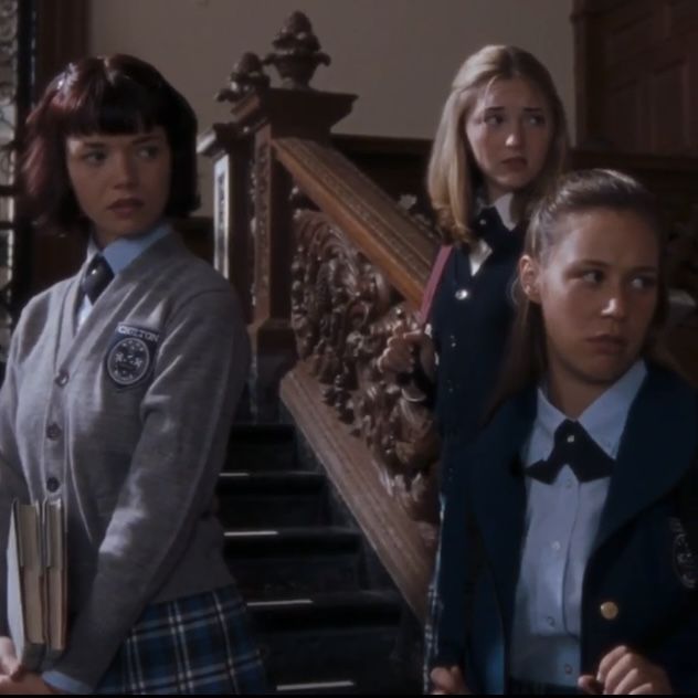 three girls in school uniforms are standing on the stairs