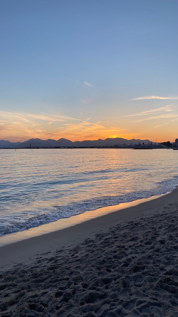 the sun is setting at the beach with mountains in the distance