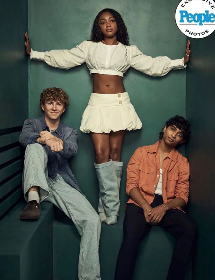 two men and a woman sitting on top of a set of stairs in front of a green wall