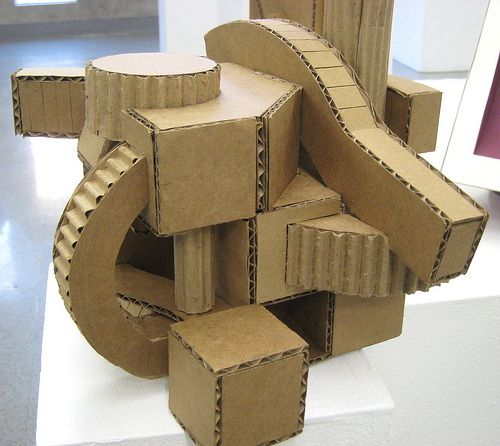 a sculpture made out of cardboard boxes sitting on top of a white table next to a framed photo