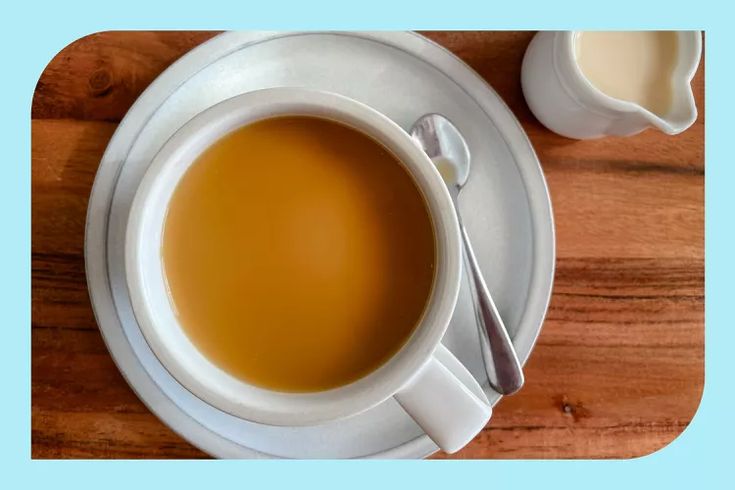 there is a cup of tea next to a spoon on a plate with milk in it