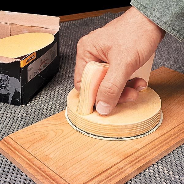 a person is using a sanding disc on a piece of wood with a box in the background